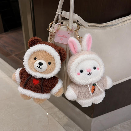 Brown teddy bear and white bunny plush bag charms hanging from a light-coloured handbag
