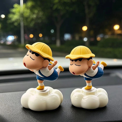 Two Shinchan figures in yellow hats balancing on light cloud bases on a car dashboard