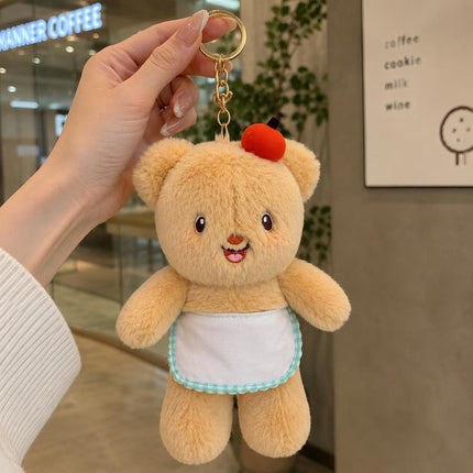 Light tan plush teddy bear bag charm with red apple and light apron hanging from a gold-tone ring