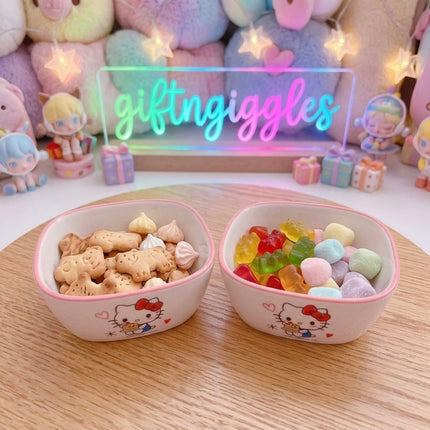 Two Hello Kitty bowls with pink rims shown holding snacks and sweets
